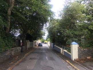 The eastern side of the road is a combination of low walled gardens and hardstanding parking areas in front of the houses to the south of the site, with walled gardens and soft