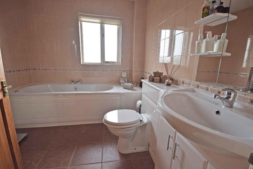 White suite comprising a panel enclosed jacuzzi bath with mixer tap and tiled wall surrounds, fully tiled corner shower cubicle with fitted shower and chromium fitments, low level wc with concealed