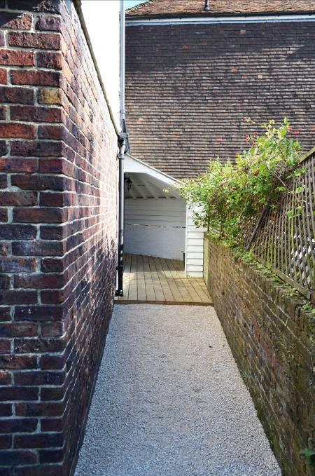 To the side of the house a gravelled pathway leads to a shallow decked terrace partially set beneath a timber framed canopy and providing access to an external utility cupboard with plumbing for