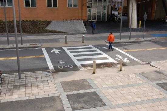 Where they cross, consider using a different surface treatment, such as imprinted, textured or colour concrete or asphalt, to visually define pedestrian routes.