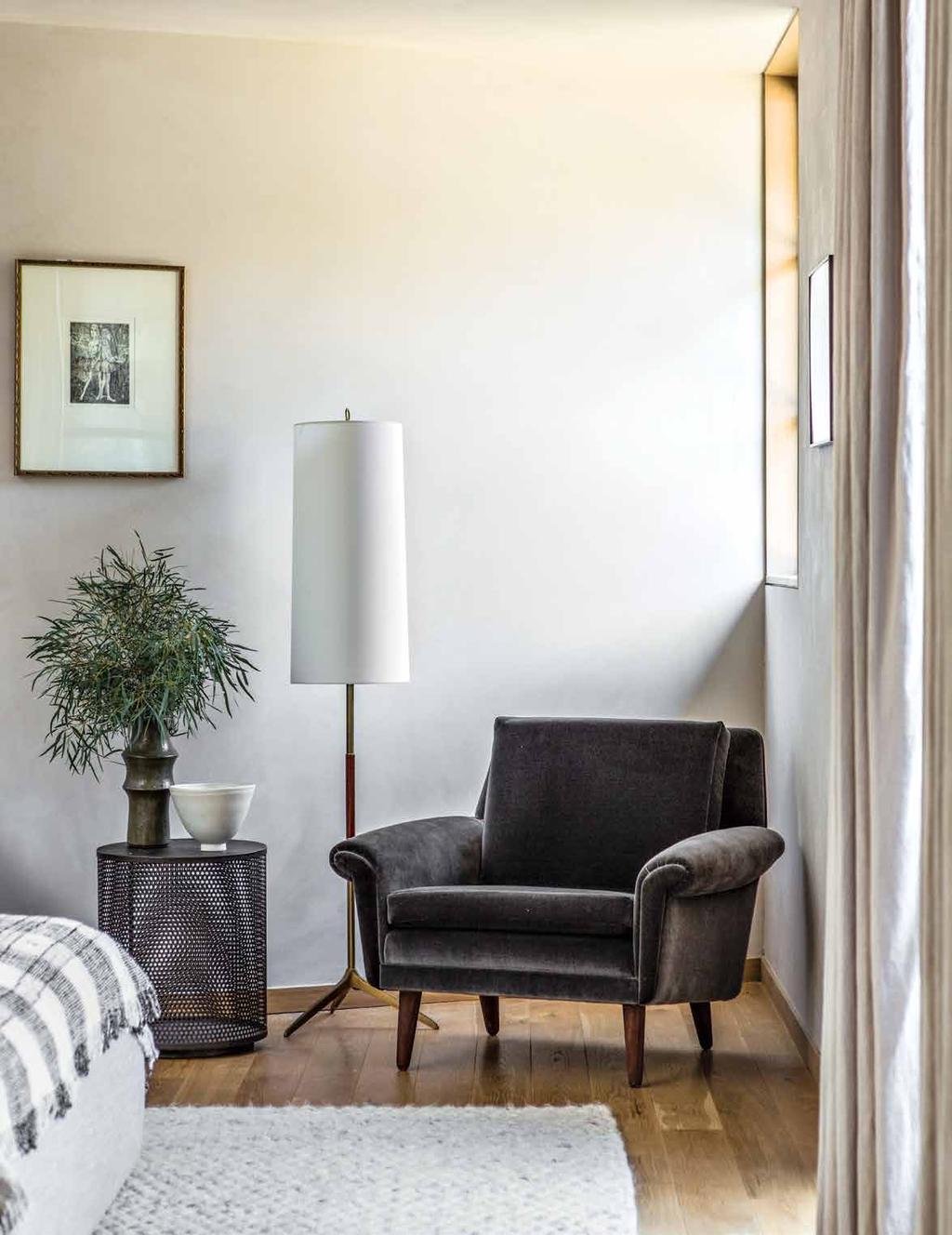 A corner of the master bedroom displays a Visual Comfort & Co. floor lamp from Circa Lighting and a metal side table from Roost. The vintage armchair is covered with velvet from Donghia.