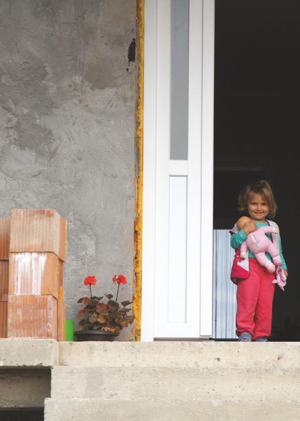 A beneficiary child in front of a house which was reconstructed thanks to a