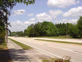Mature pines and shade trees line the corridor outside of the right-of-way. Space within the right-of-way is limited for roadside landscape elements.