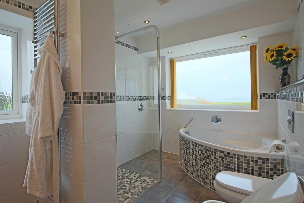 with storage cupboard below, wall hung wc, bidet and urinal. Storage cupboard, full decorative tiling to floor and walls, windows to side and to rear with sea views.