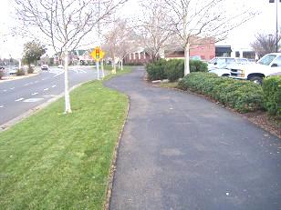 Figure 2: A wide buffer which includes a berm, bike/walk pathway, and landscaping can be used to conceal parking areas that abut a public rightof-way. c. PARKING 