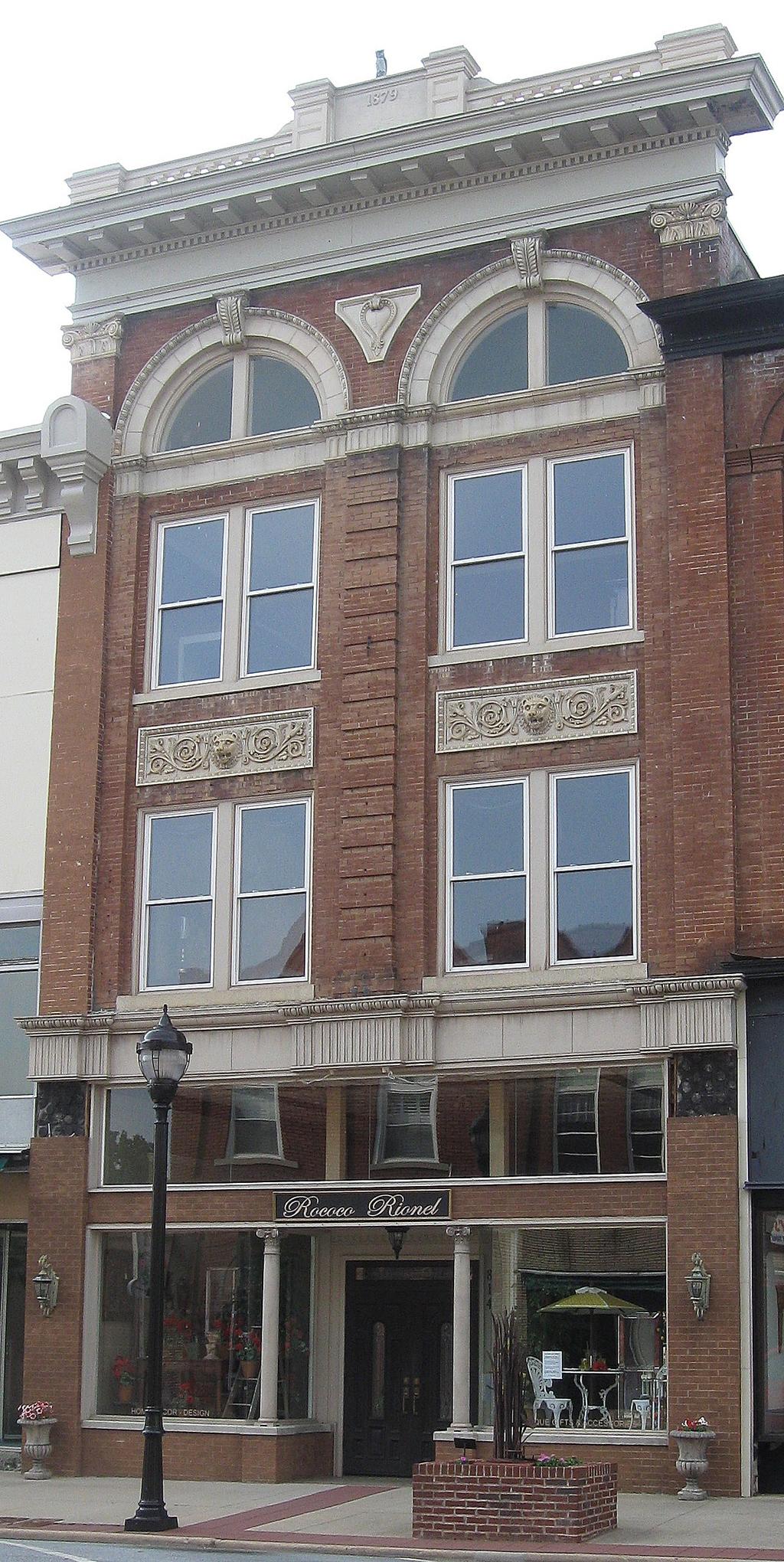 Two-story red brick commercial building with finelyexecuted three-and-one-half-story Classical Revivalstyle façade; classical stone ornament; reconstructed stepped wood parapet with a central