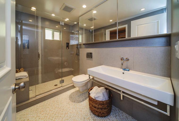A REMODELED FULL BATHROOM off the hallway features tile floor with glass tile inserts, tiled wall, sink with polished chrome faucet and polished chrome towel holder, two medicine cabinets with glass