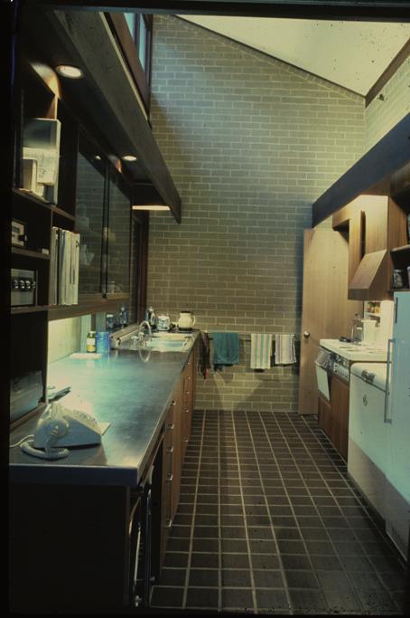 The kitchen is to the right (where the telephone handset can be seen). Right: The kitchen is a galley style with stove, deepfreezer, and refrigerator at right.