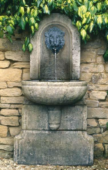 The Lion Mask Wall Fountain [item 4] A wall fountain in age patinated artificial stone, having arched back plate inset with a lead lion mask