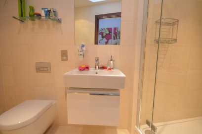 Fully tiled Antalaya cream limestone tiling to walls and floor, electric shaver point, fitted wall mirror, fitted glass shelf, chrome ladder style electric radiator, recessed ceiling spotlights and