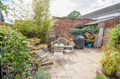 stocked beds with a low brick wall, sandstone coping and metal railings There is also a brick sett driveway with double opening metal gates Outside lantern style light and gas meter