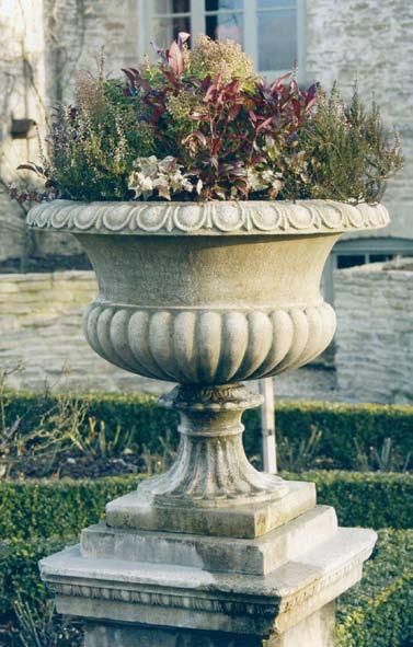 The Hevingham Hall Terrace Urn [item 47] A classical age patinated artificial stone Tazza urn having semi-lobed body with everted rim, raised upon a fluted socle on a square base.