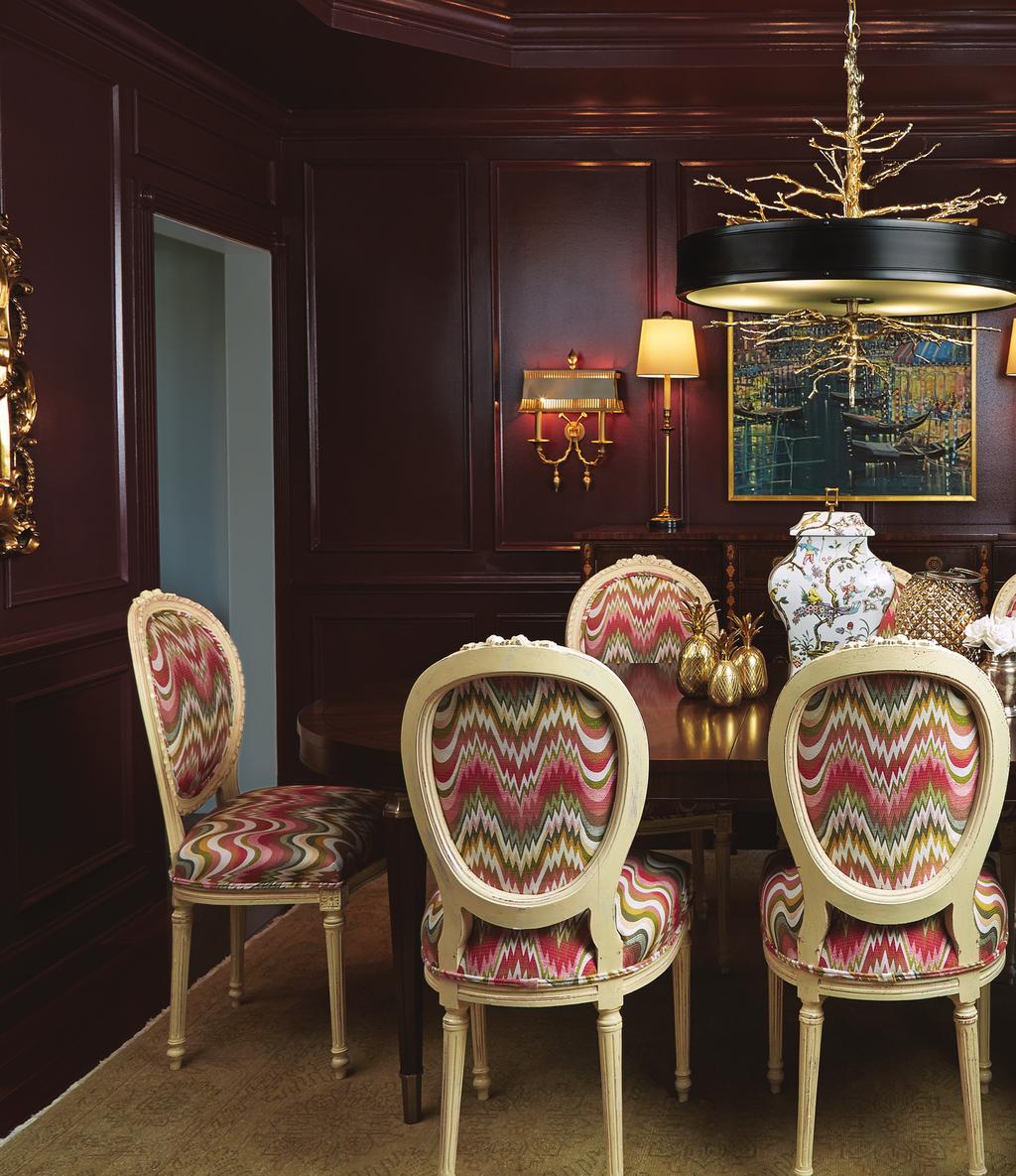 The lacquered, Marsala-colored walls and the table s burl-wood finish in the dining room create an intimate, warm atmosphere, contrasted by the lively, colorful pattern on the fabric of the Louis