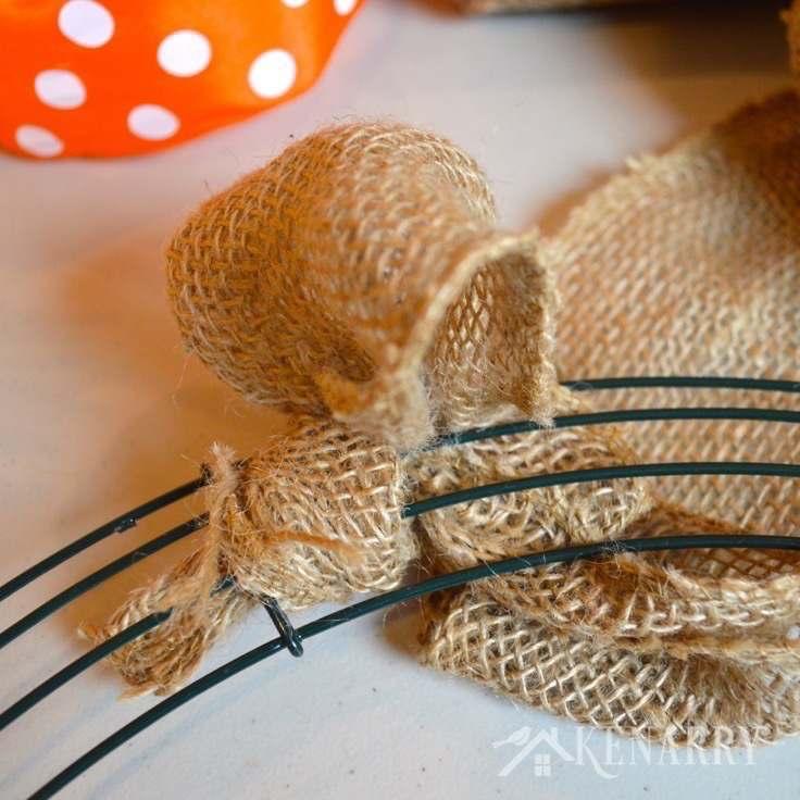 2. Begin weaving the burlap ribbon through the wire frame. Flip the wire frame around so the top faces you now and the knot you just made is in the back.