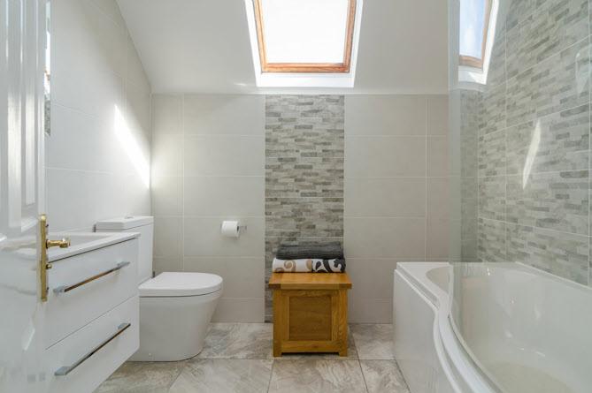 FULLY TILED BATHROOM: White suite comprising panelled bath with mixer tap and shower over, low flush wc, vanity unit, fully tiled walls, tiled floor, low