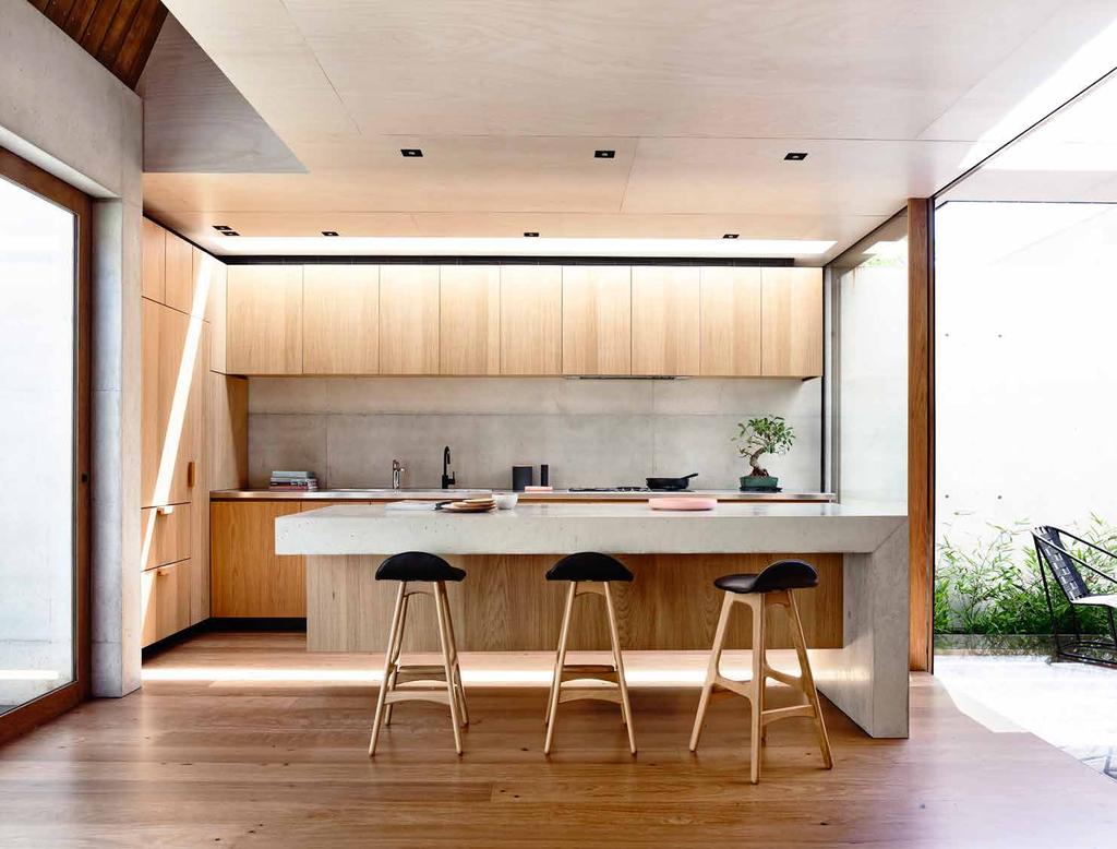 Off-form concrete extends into the kitchen with a cantilevered concrete benchtop and splashback The workbench is stainless steel, and timber is used in the tall timber box housing for the fridge,