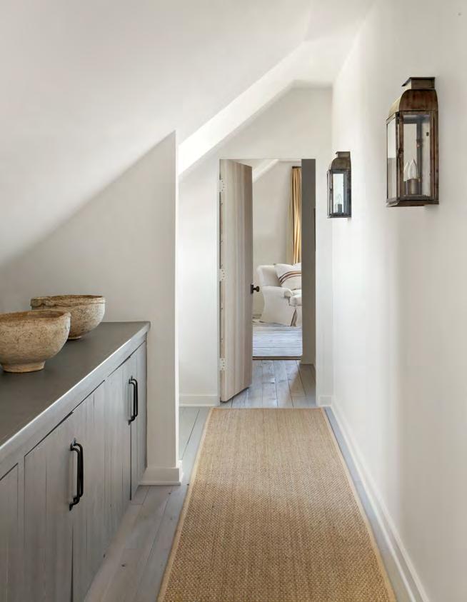 A seagrass runner lines the upstairs hallway. Iron sconces and painted cabinets are designed by Cummings.