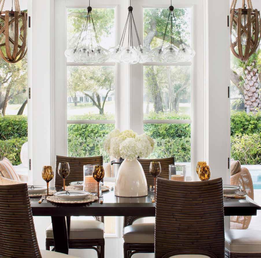 The bright dining room, flooded with sunlight through ample windows and doors, features rattan chairs by Palecek around a custom-designed dark