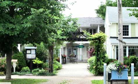 A plaza in Bayfield contains an outdoor cafe and various shops. The entrance is embellished with a vined archway.
