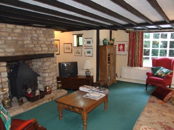 Sitting Room measuring approximately 17 6 x 14 8 minimum (5.33m x 4.47m) with exposed ceiling timbers. Stone fireplace with wood burning stove inset, stone hearth, alcoves to either side, shelving.