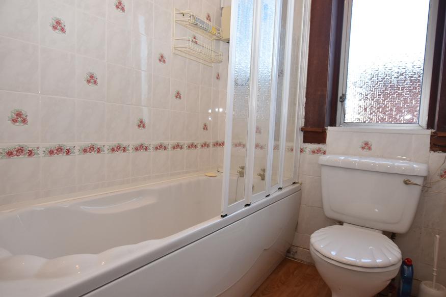 BATHROOM with window to the rear. White suite. Shower over bath with screen. Tiled behind bath.