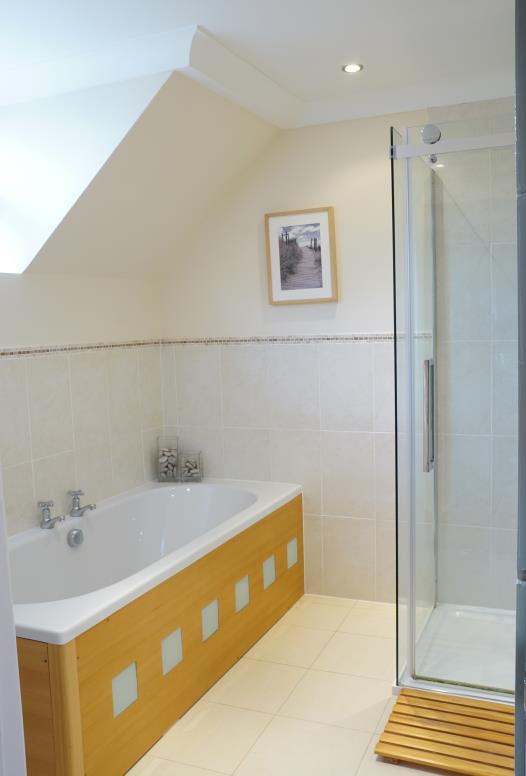 Family Bathroom comprising timber panelled bath with hot and cold taps. Ceramic tile surrounds. Walk-in shower over shower tray. Sliding glazed shower door and glazed screens.