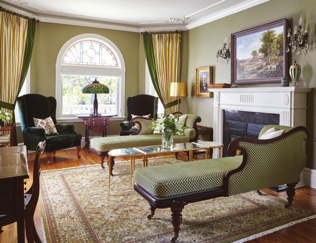 A dramatic pair of cream and moss green silk drapes flank the arched window. Emerald green velvet armchairs and a stained glass and bronze Tiffany lamp create a cosy vignette in the bay window.