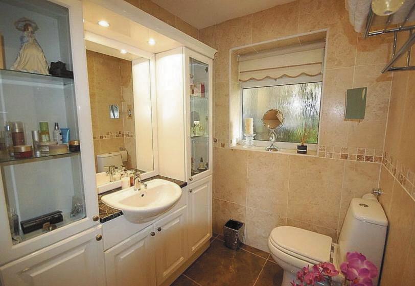 En suite Having Travertine style tiling to the walls and fully tiled floor, 2 piece suite comprising low flush toilet, vanity wash basin with cupboards beneath and inset lighting above, chrome ladder