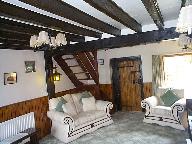 SITTING ROOM: about 17 10 x 12 6 max with heavy beamed ceiling, stone ornamental fireplace with raised hearth, two radiators, wall lighting points, half timbered walls, ledged and braced cottage