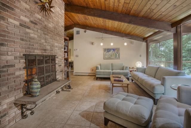 The dramatic living room, with floor to ceiling brick fireplace, tongue and groove cedar ceilings, and walls of windows that