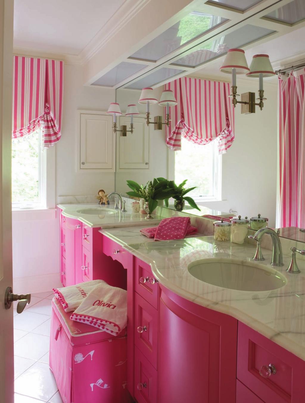 A fun departure from the dominant color scheme, this bright pink bathroom features such details as mirror mounted sconces, crystal cabinet knobs, bow front vanities with a marble top, and a whimsical